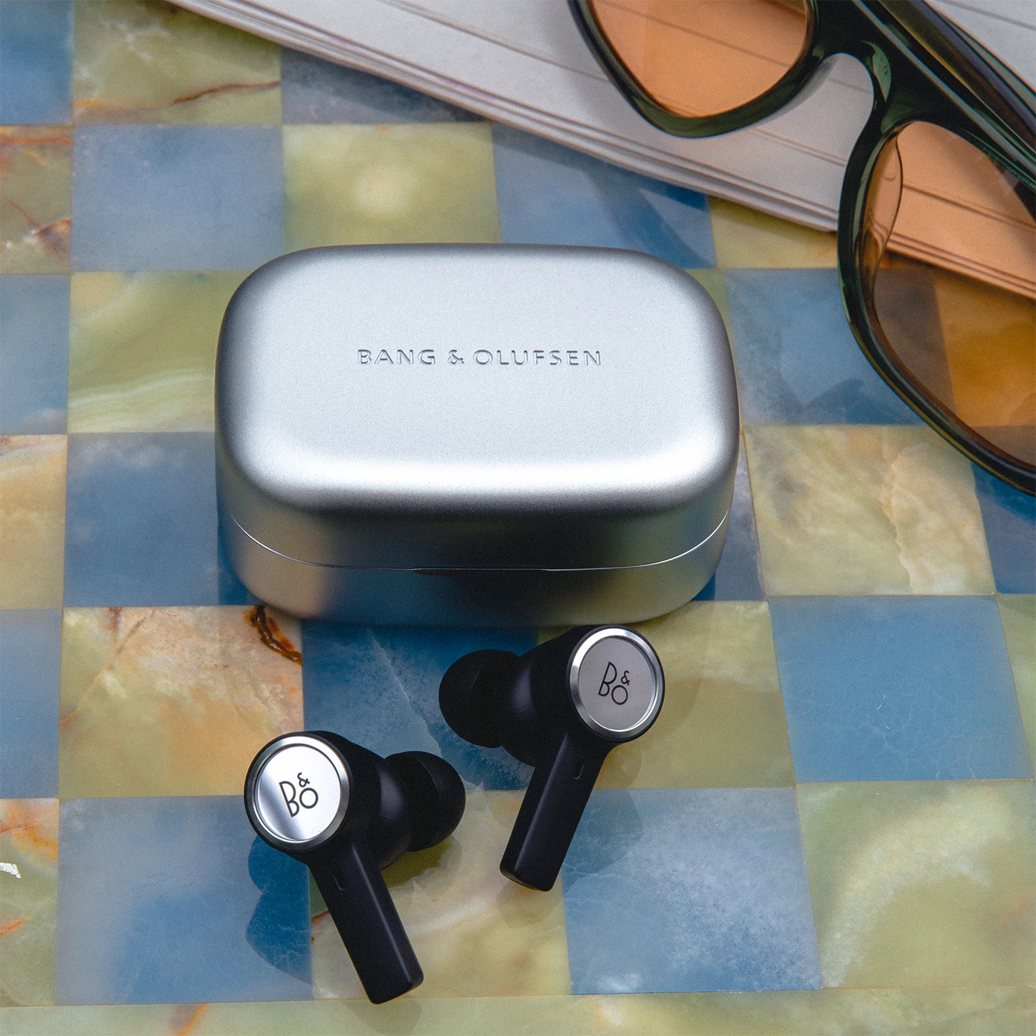 Beoplay Eleven on a checkered table with sunglasses on the side