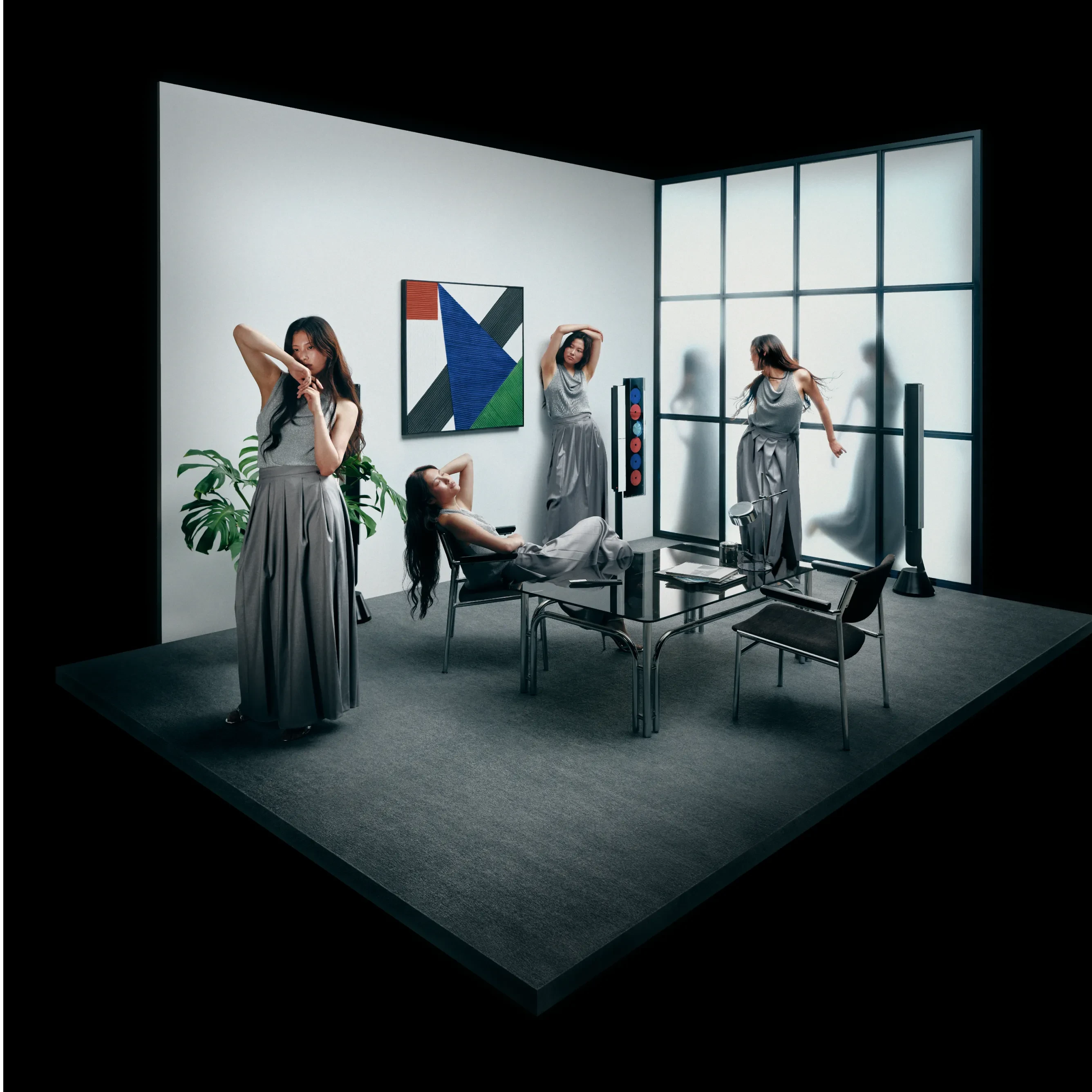 Models in gray dresses pose in minimalist set with geometric artwork, modern furniture, Beosystem 9000c and large windows.