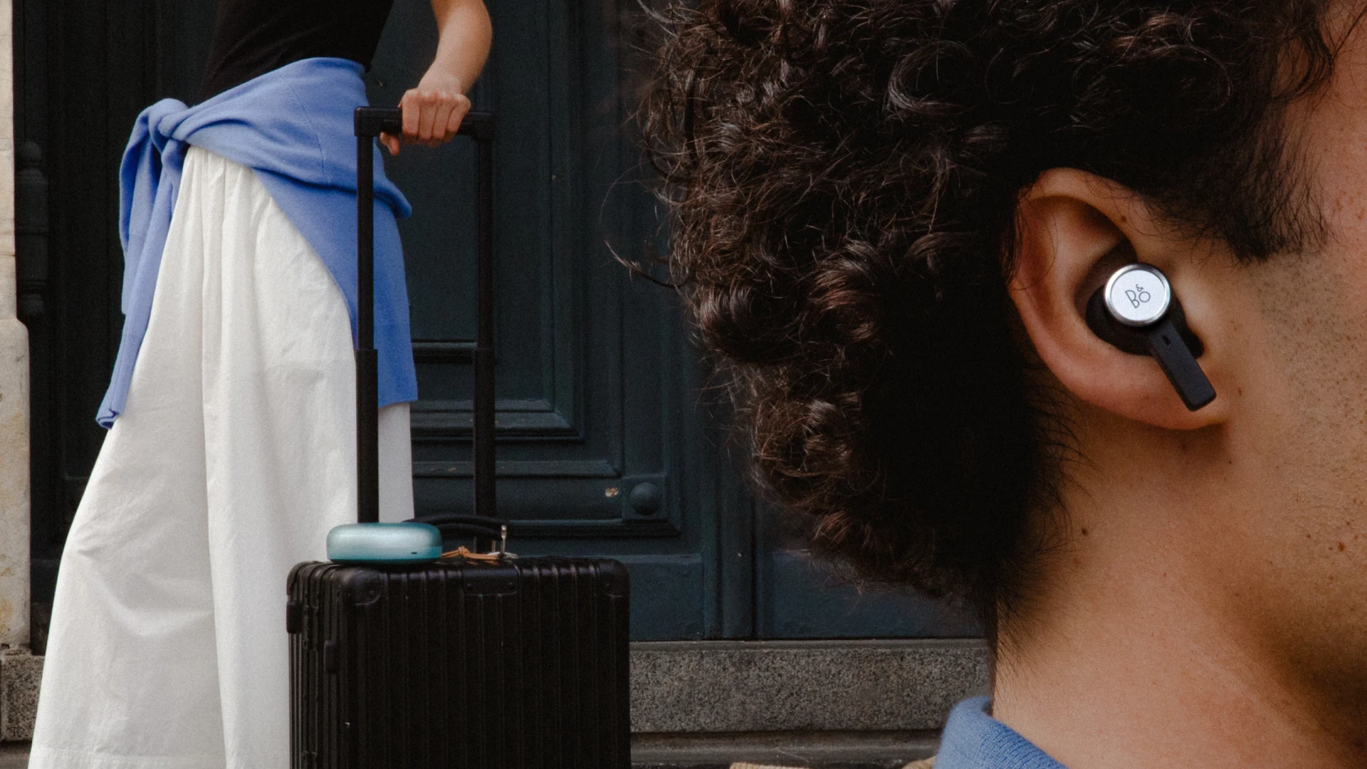 Beosound A1 3rd Gen Eucalyptus Green on a luggage a woman is holding and a close up of a side face of a guy who is wearing Beoplay Eleven