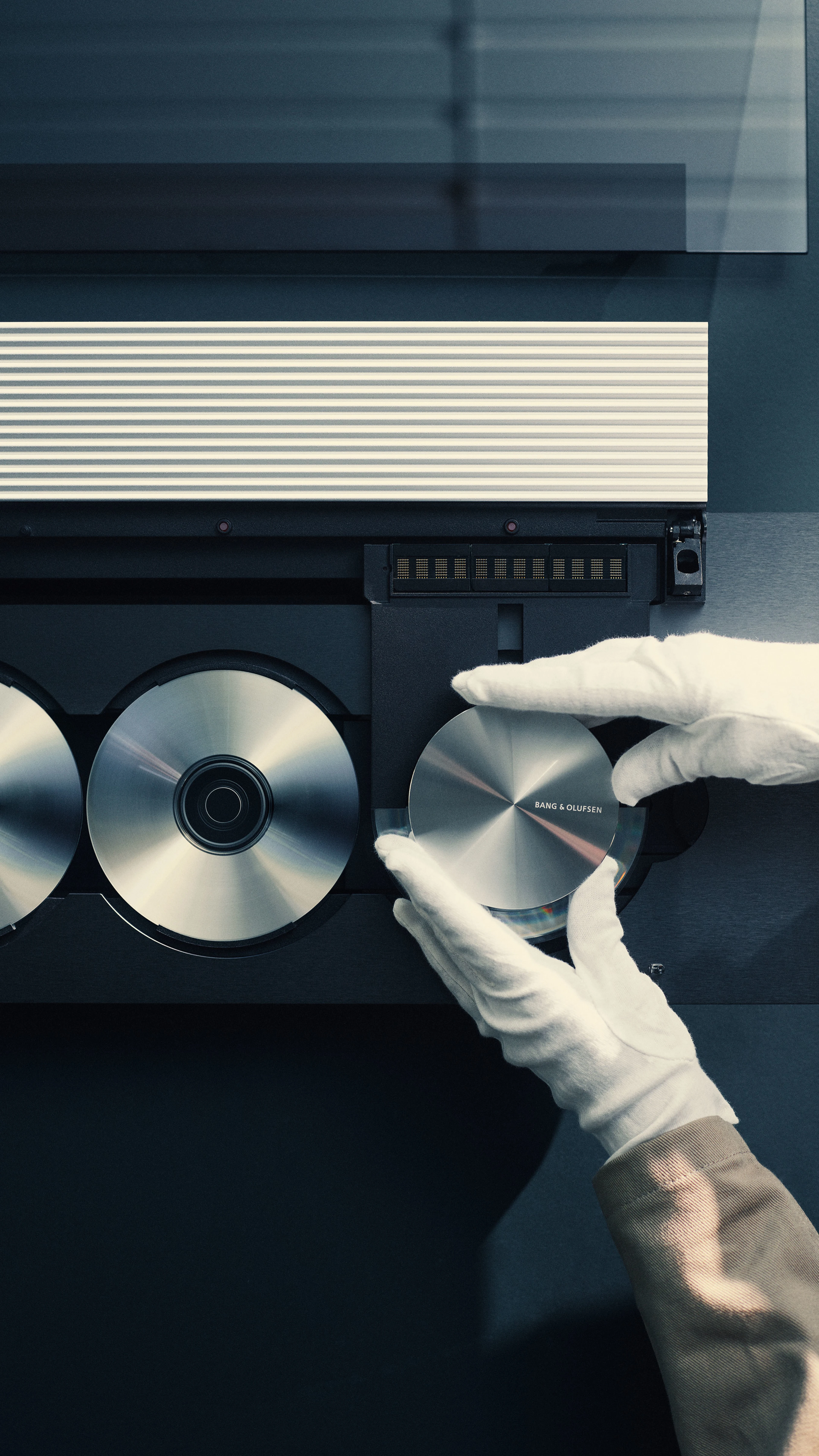 Detail image of a pair of hands in white gloves adjusting a Beosound 9000 CD player recreated as the Beosystem 9000c in Factory 3, Struer