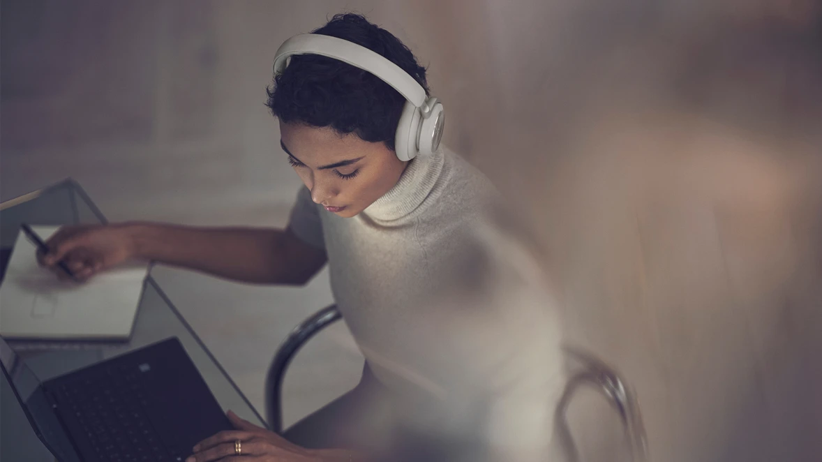 A woman sitting down with the headphones Beoplay HX on, while she works