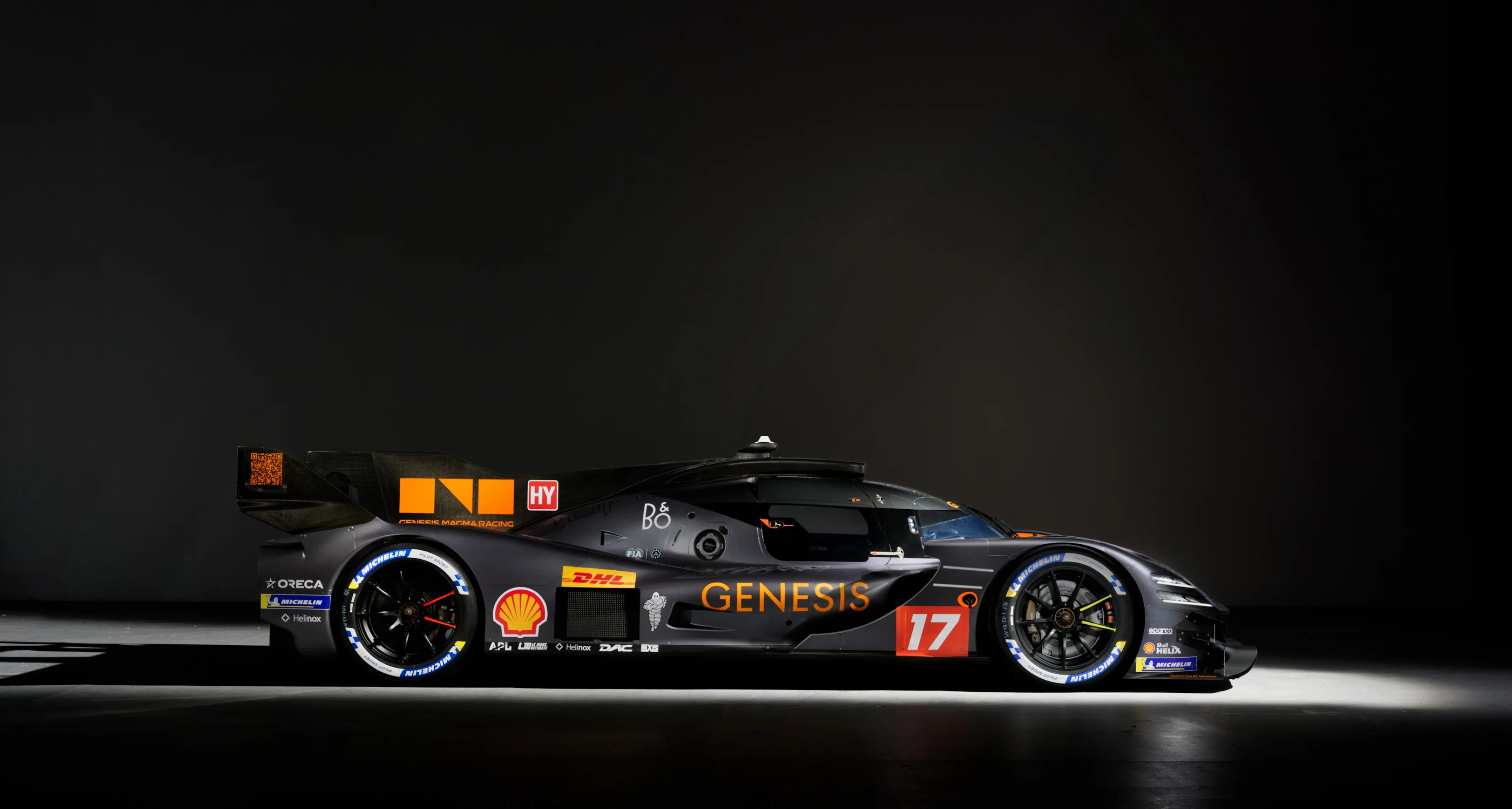 Un coche negro de Genesis Magma Racing iluminado de forma espectacular sobre un fondo oscuro que resalta su silueta aerodinámica y su carrocería brillante
