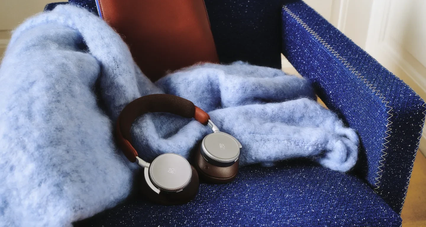 Beoplay H100 in the variant Century Brown on a blue armchair with cozy woolen blanket