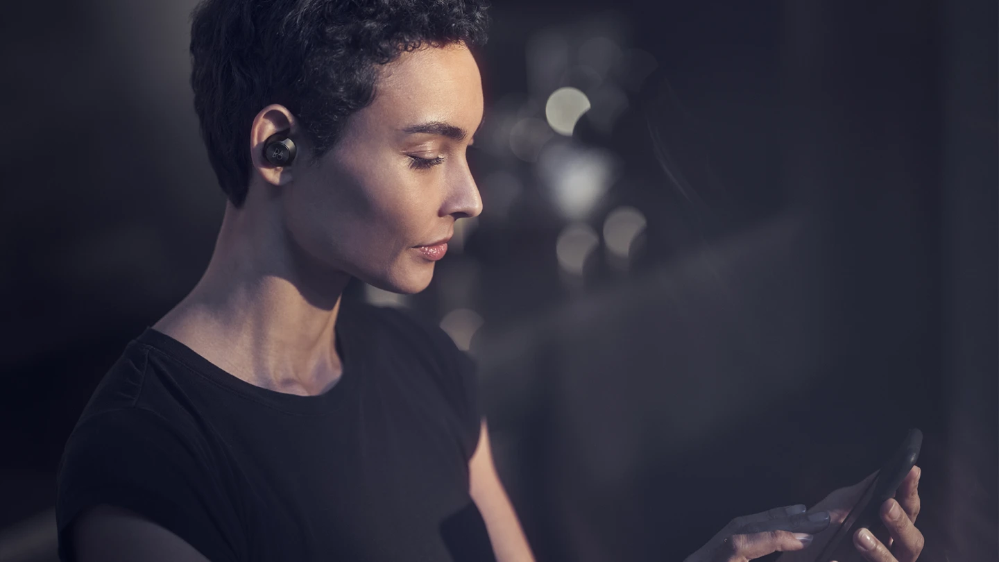 A woman wearing Beoplay EQ while she's using her smartphone