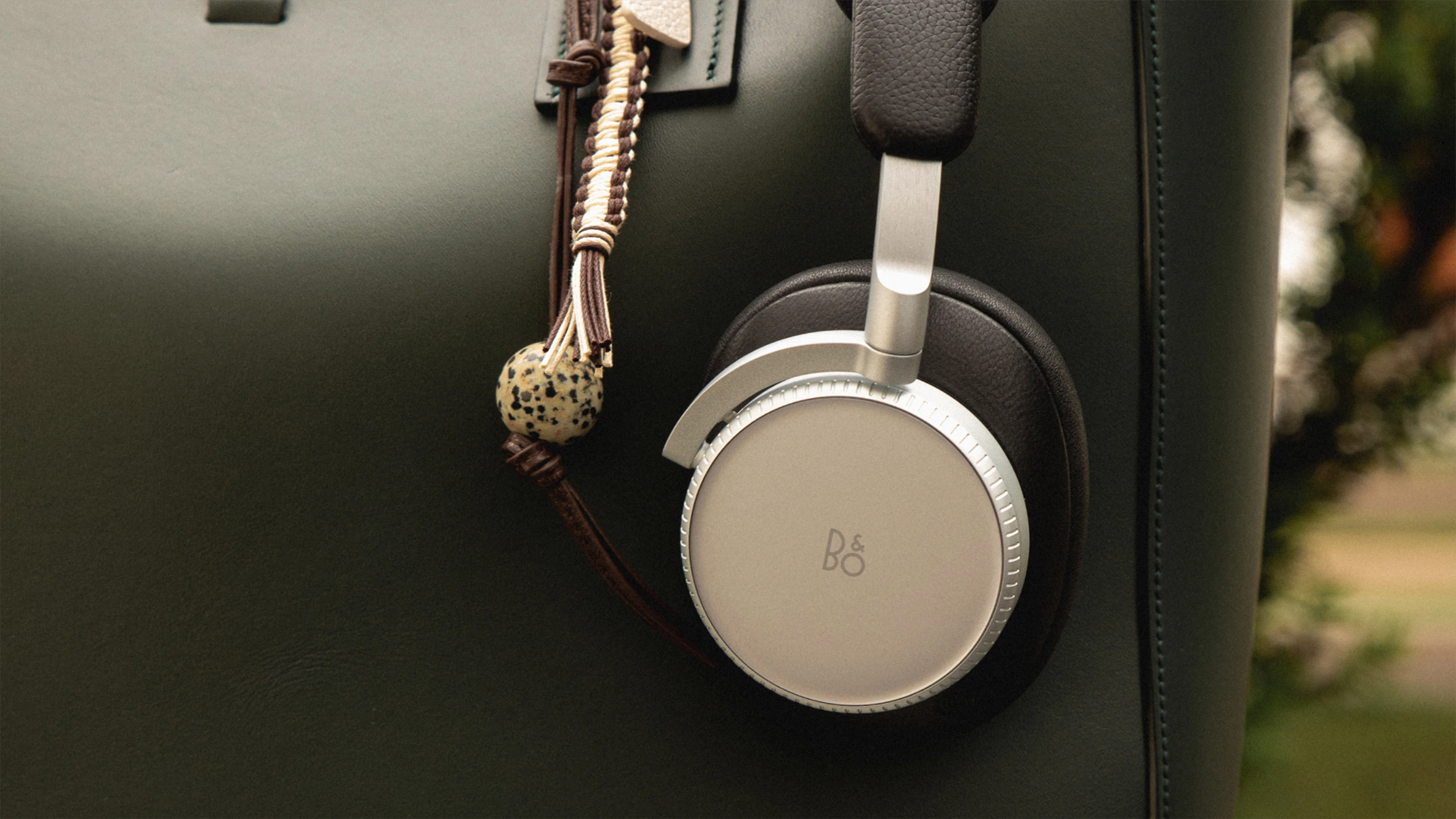Beoplay H100 black color hanging on a black leather bag