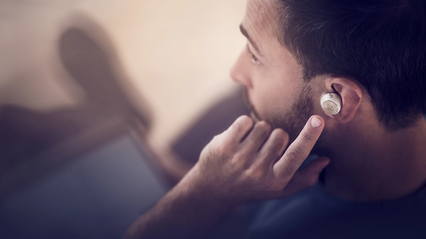 A man using the touch control on his left Beoplay EQ earbud