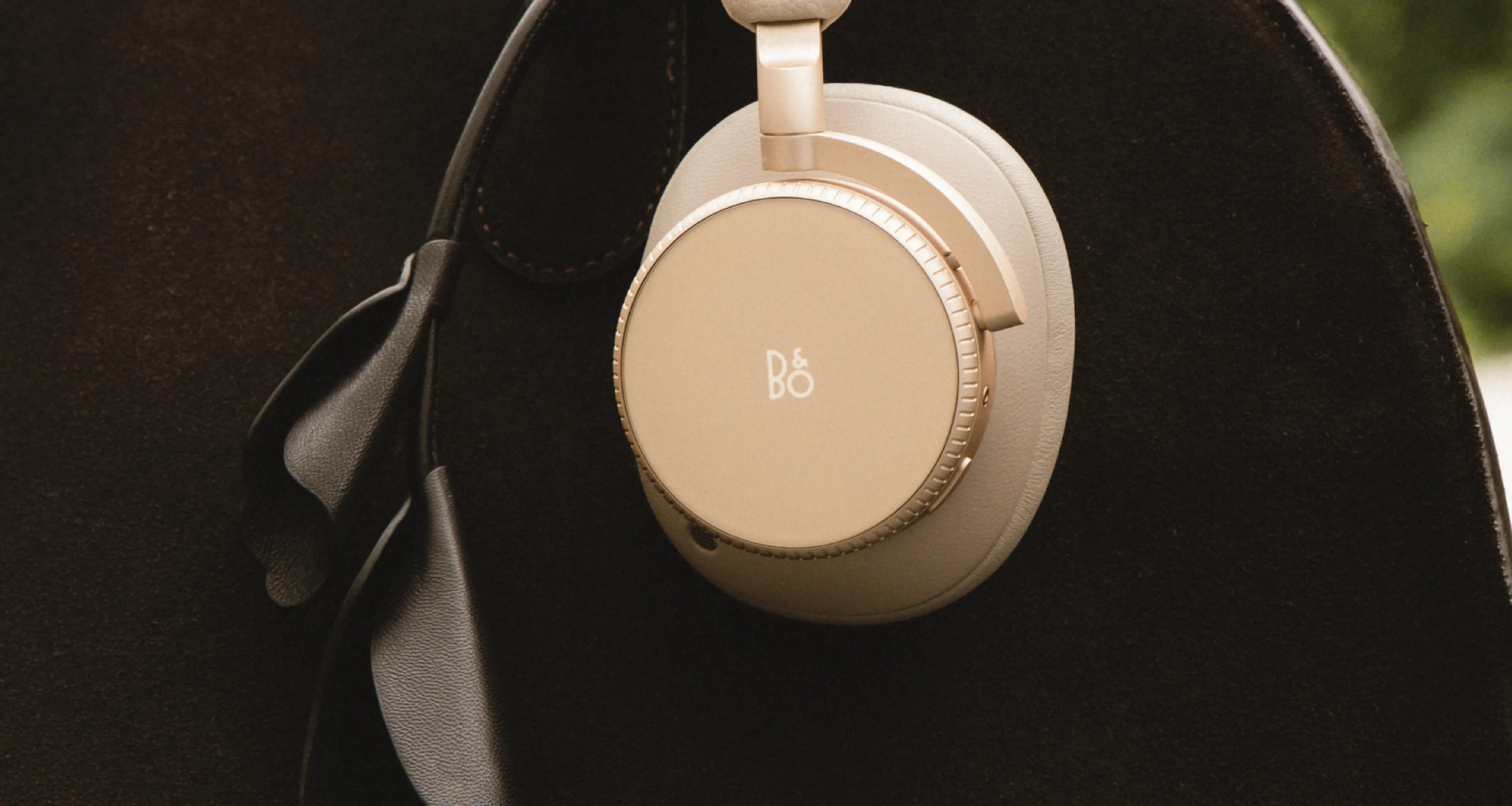 Beoplay H100 hourglass sand color hanging on a black leather bag