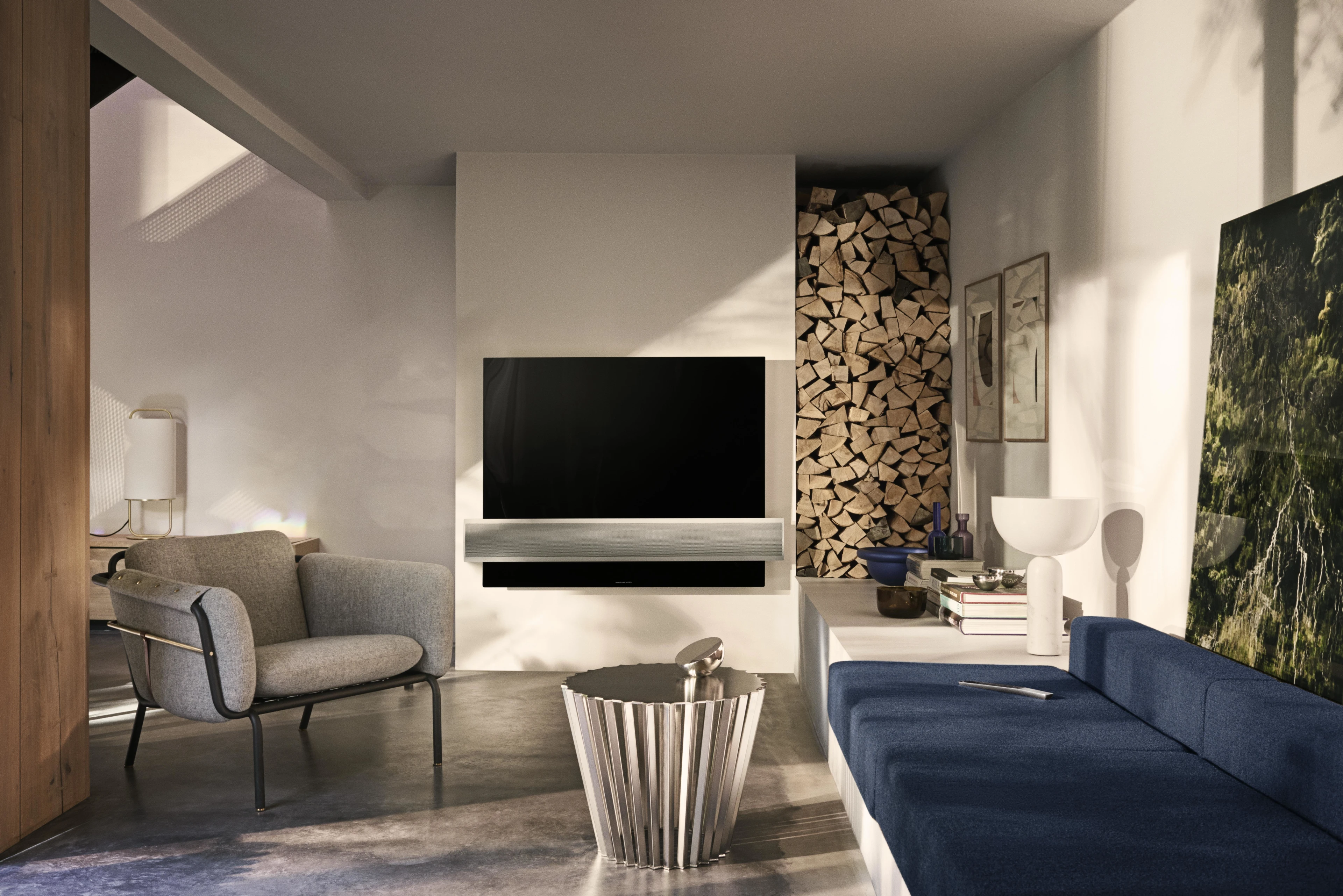 Téléviseur Beovision Eclipse dans un salon avec un canapé bleu et un tas de bois coupé