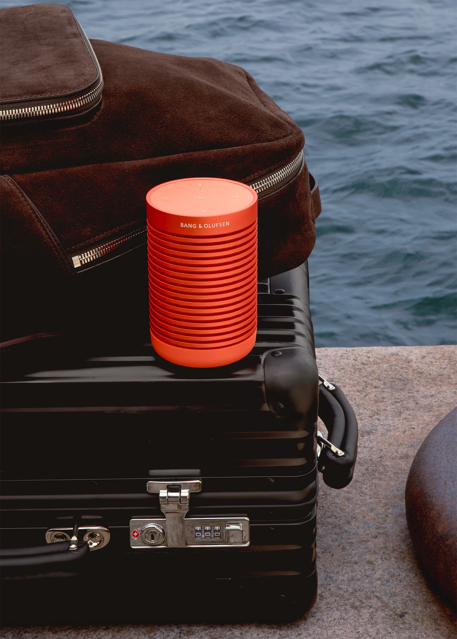 Beosound Explore orange on a black Rimowa suitcase