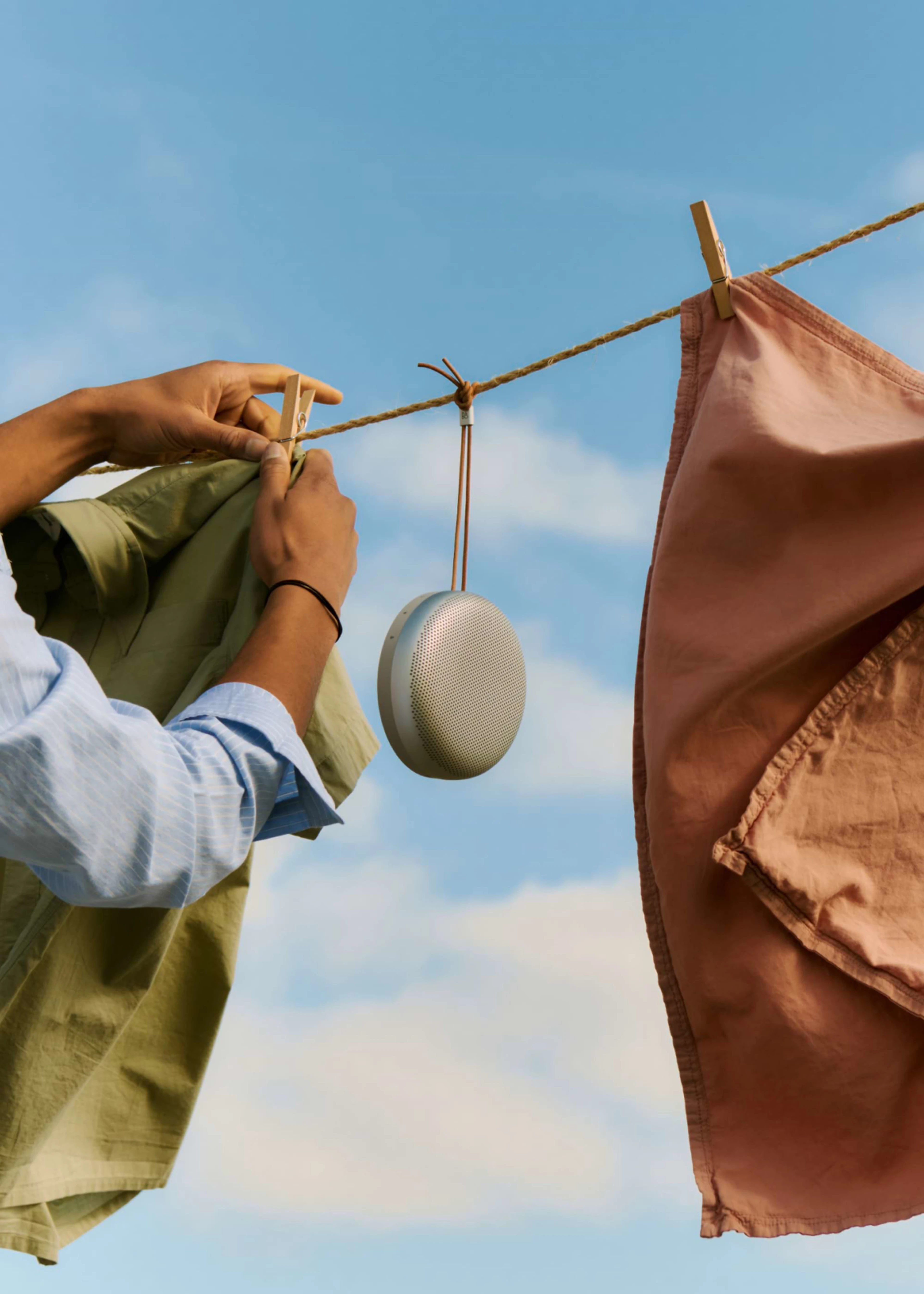 Person hanging laundry with the Beosound A1 3rd Gen