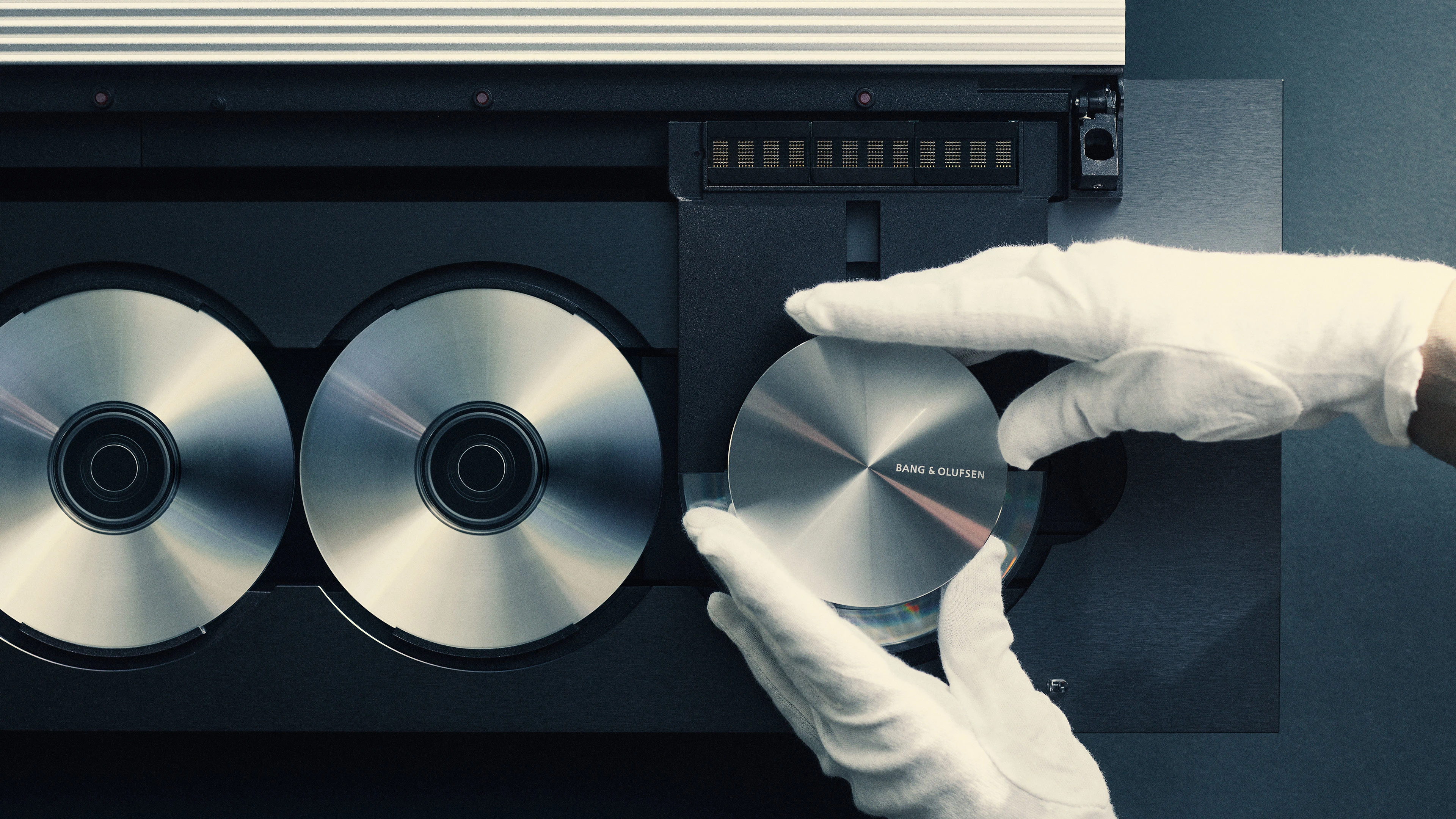 Detail image of a pair of hands in white gloves adjusting a Beosound 9000 CD player recreated as the Beosystem 9000c in Factory 3, Struer