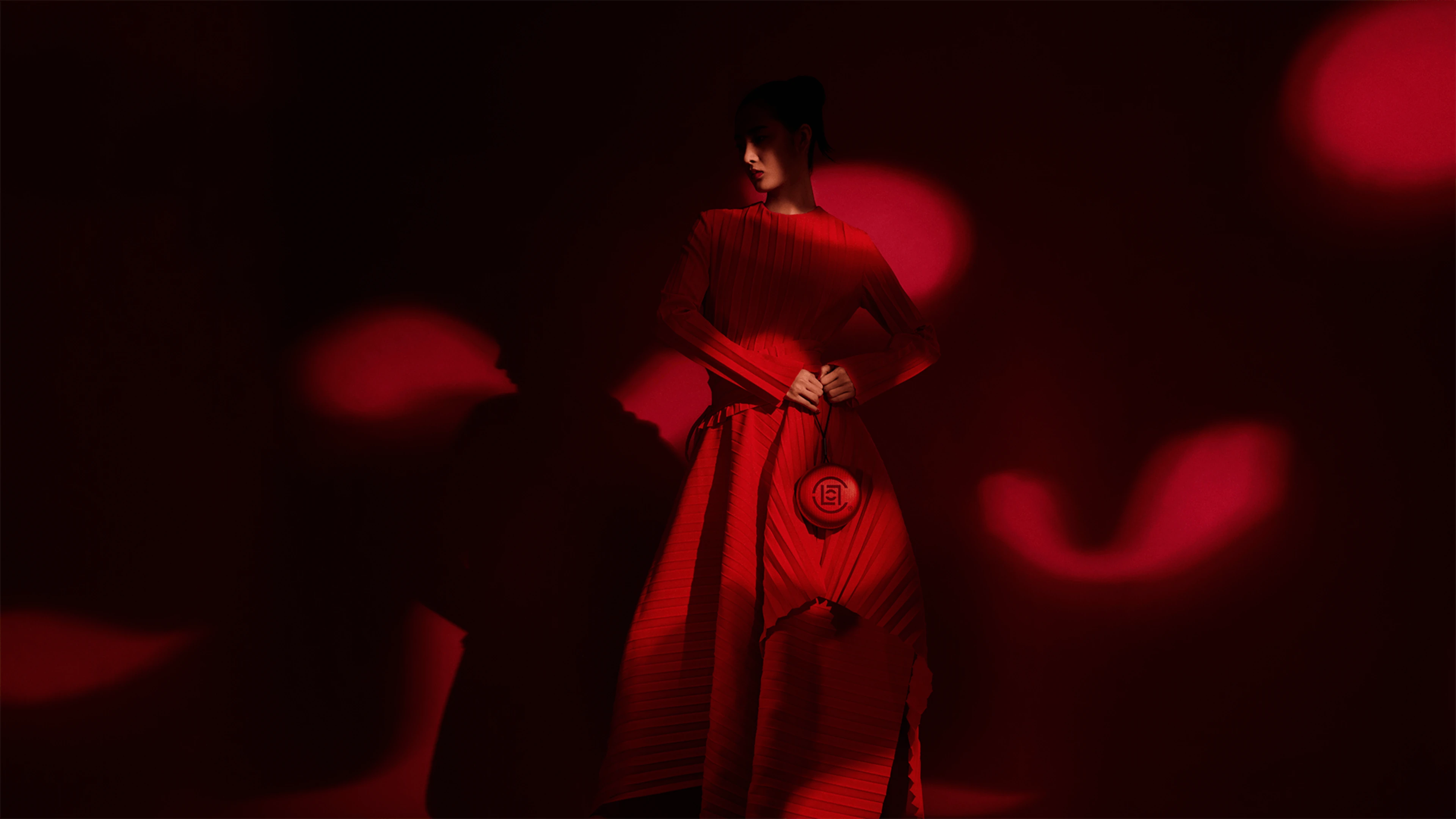Beosound A1 Clot edition with female model in a striking red pleated dress