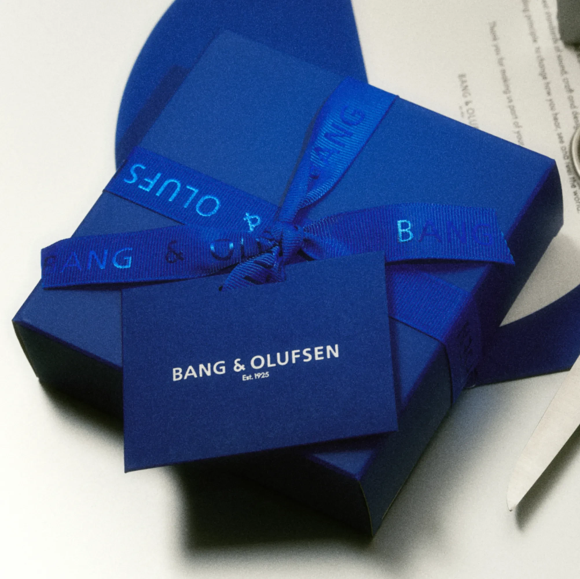 A Bang & Olufsen gift box in signature Century Blue with a matching ribbon and a logo-bearing message card attached