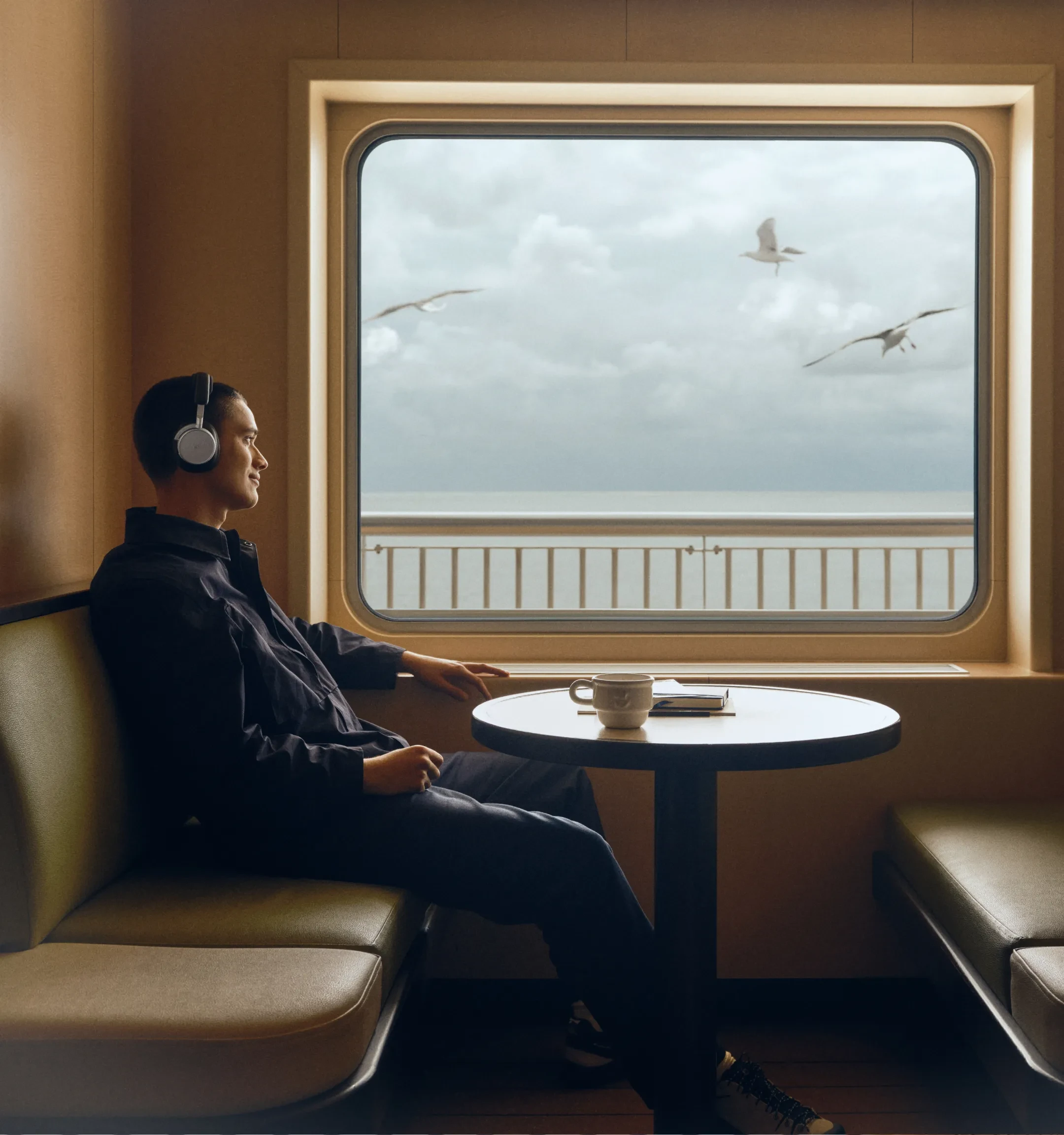 A man wearing Beoplay H100 enjoying his ride in the train, looking out of the window.