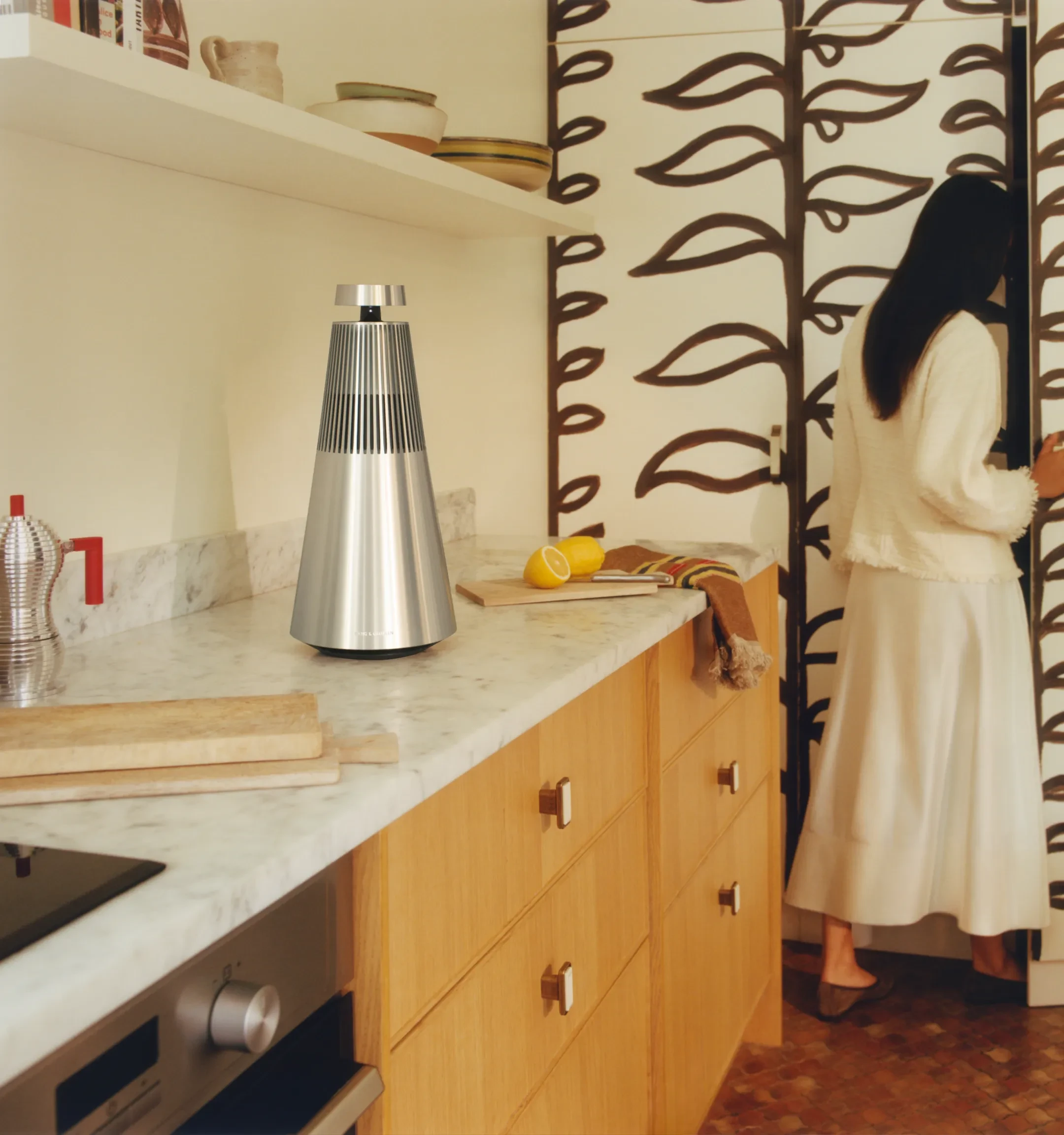 Beosound 2 竖直摆放在一间现代风格厨房的台面上，一位女士站在旁边。