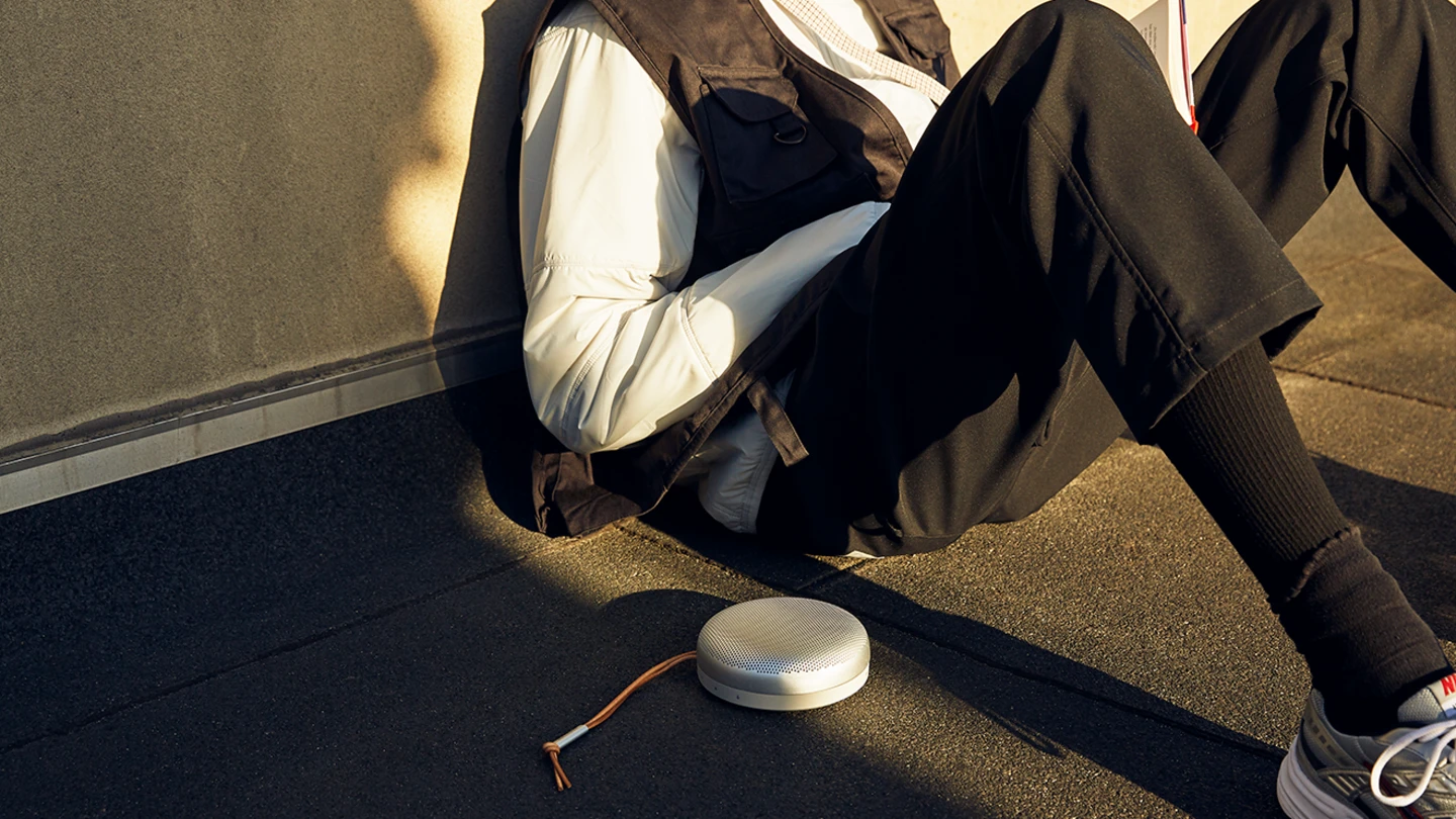 A guy is reading a book on the floor, listening to Beoosund A1 in grey mist