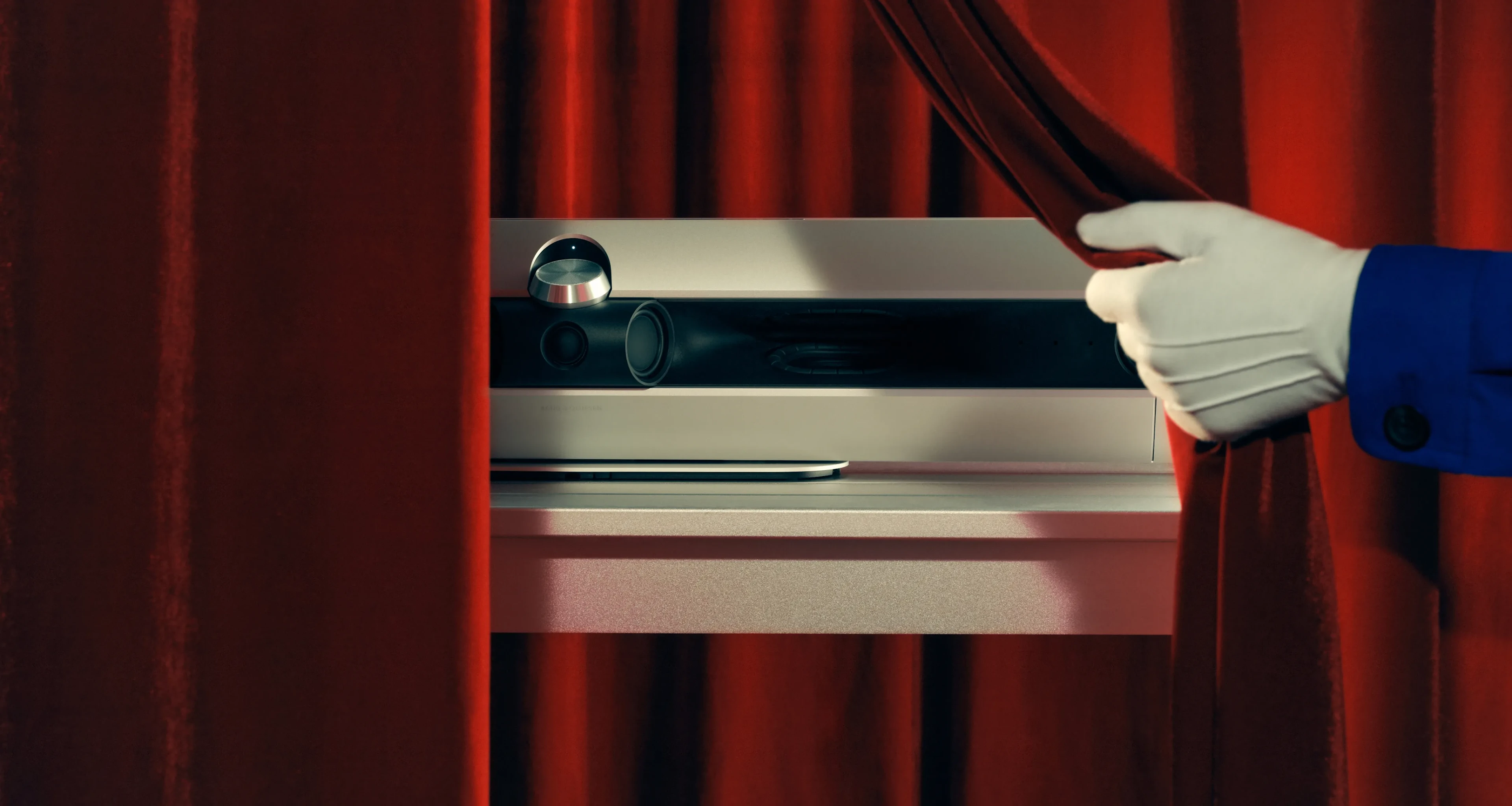 Part of Beosound Premiere soundbar being shown as someone's hand with white gloves opens the red curtain