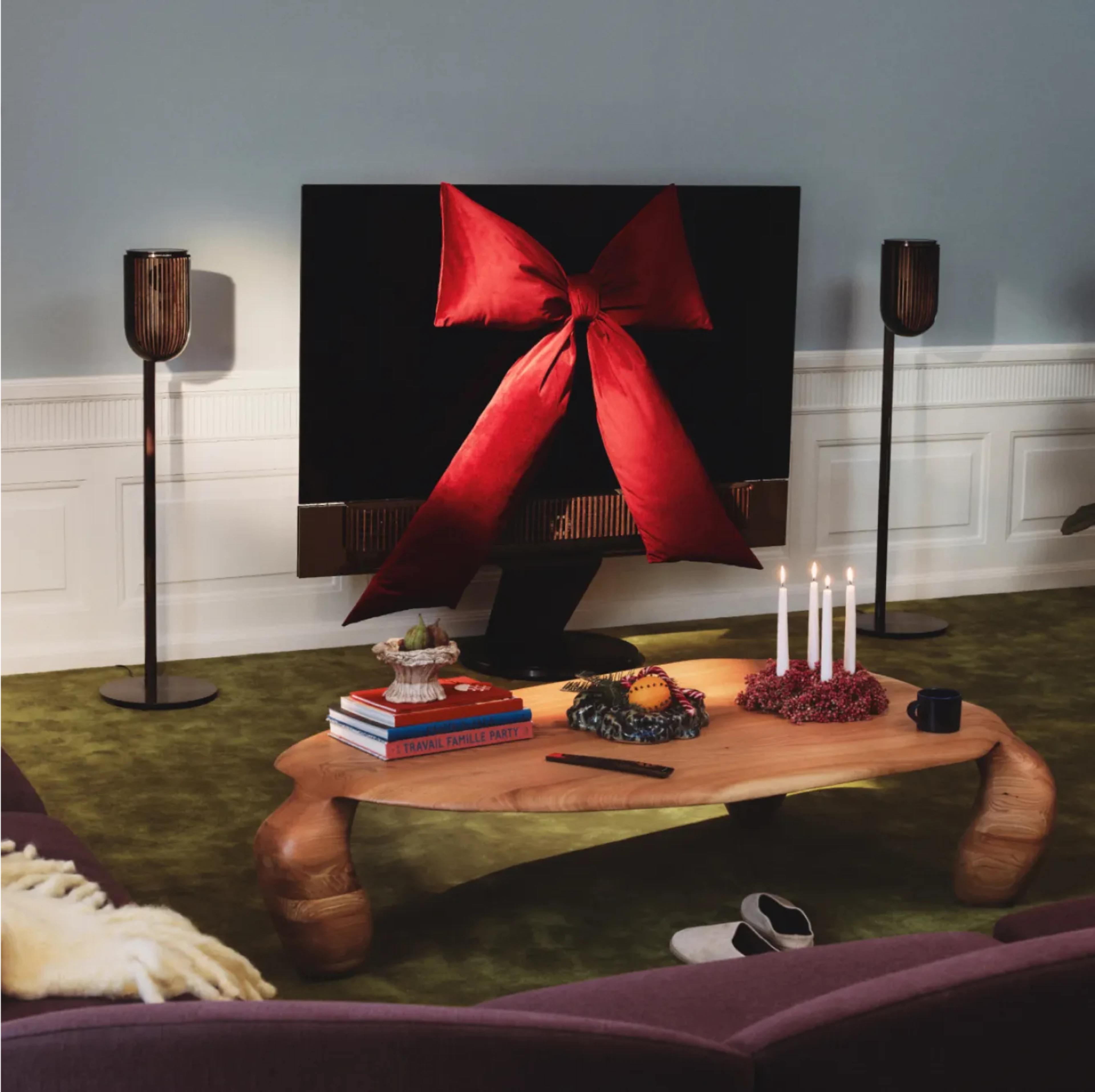Beovision Theatre TV decorated with large red bow, Beolab 8 speakers, wooden coffee table with books and lit candles, green carpet and modern floor lamps.