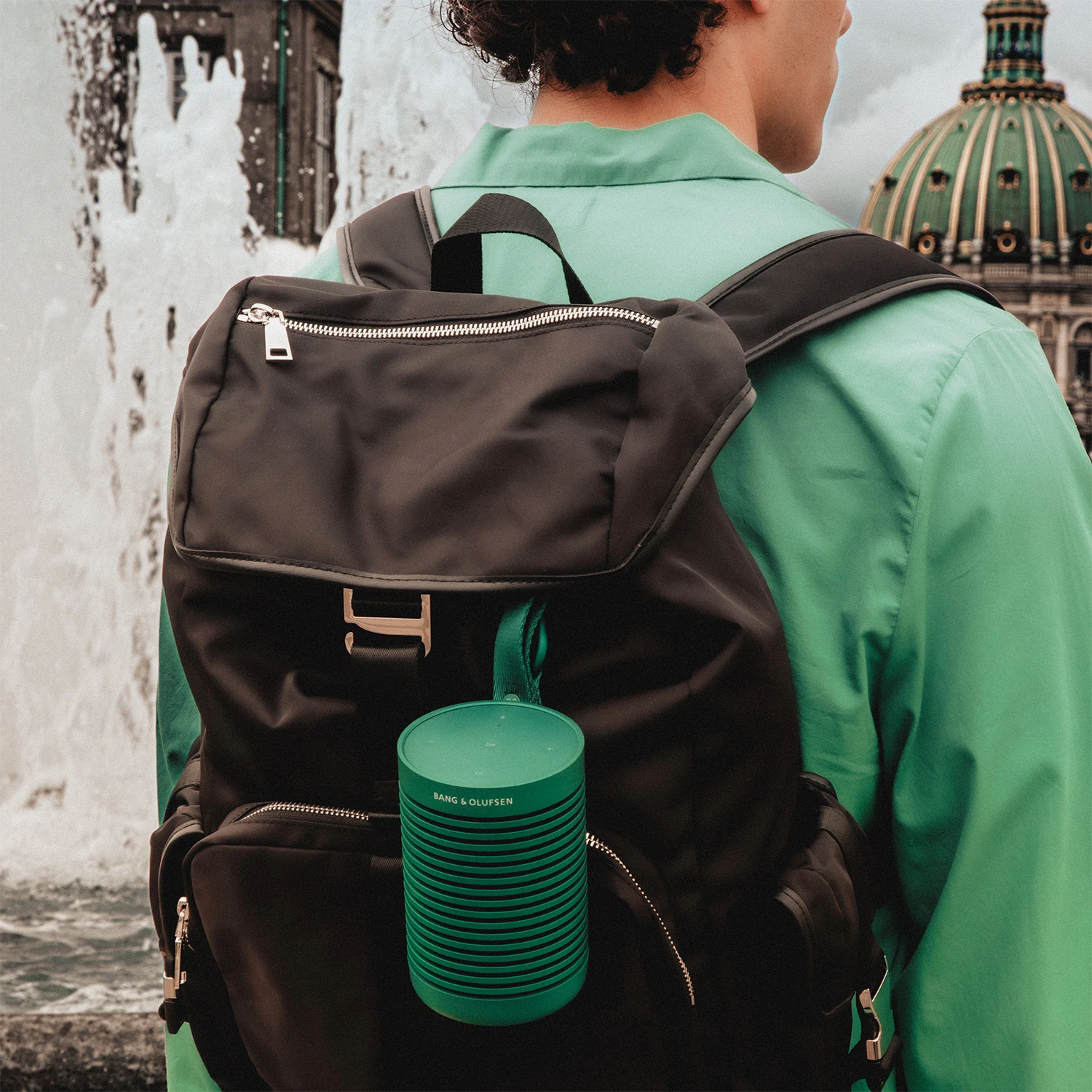 Man wearing a black backpack with Beosound Explore green speaker attached to it