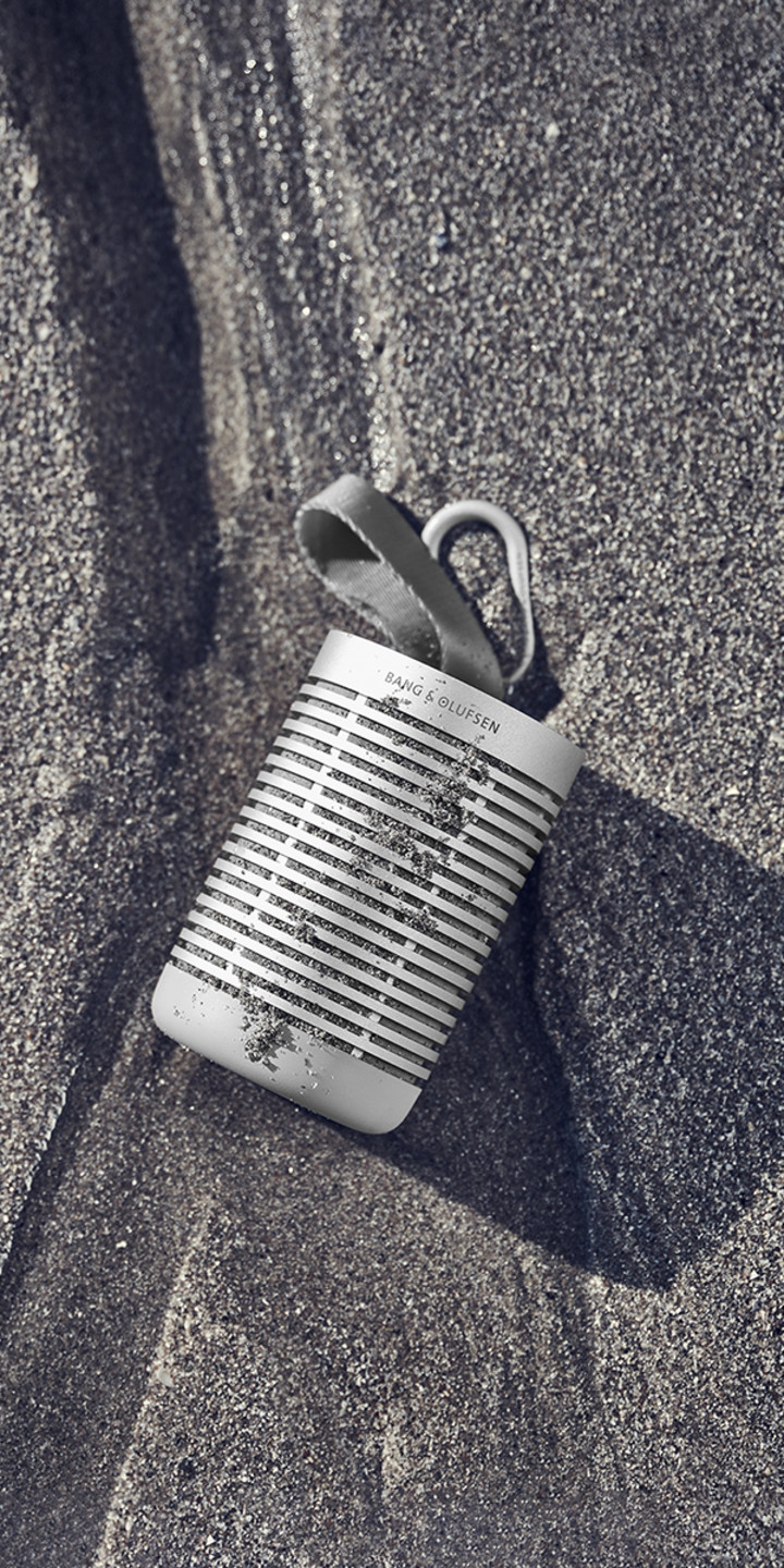 Beosound Explore placed on a beach, covered by sand