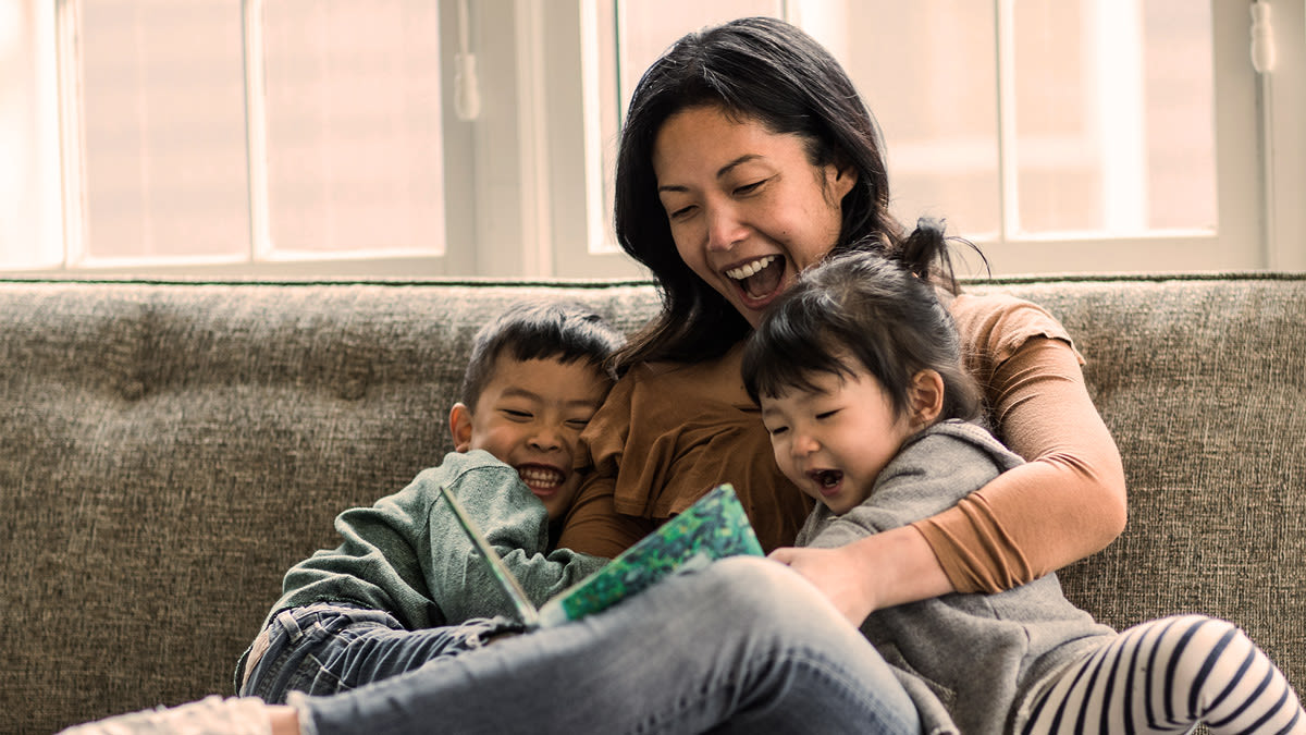 Mother and two children sitting on a couch reading a book