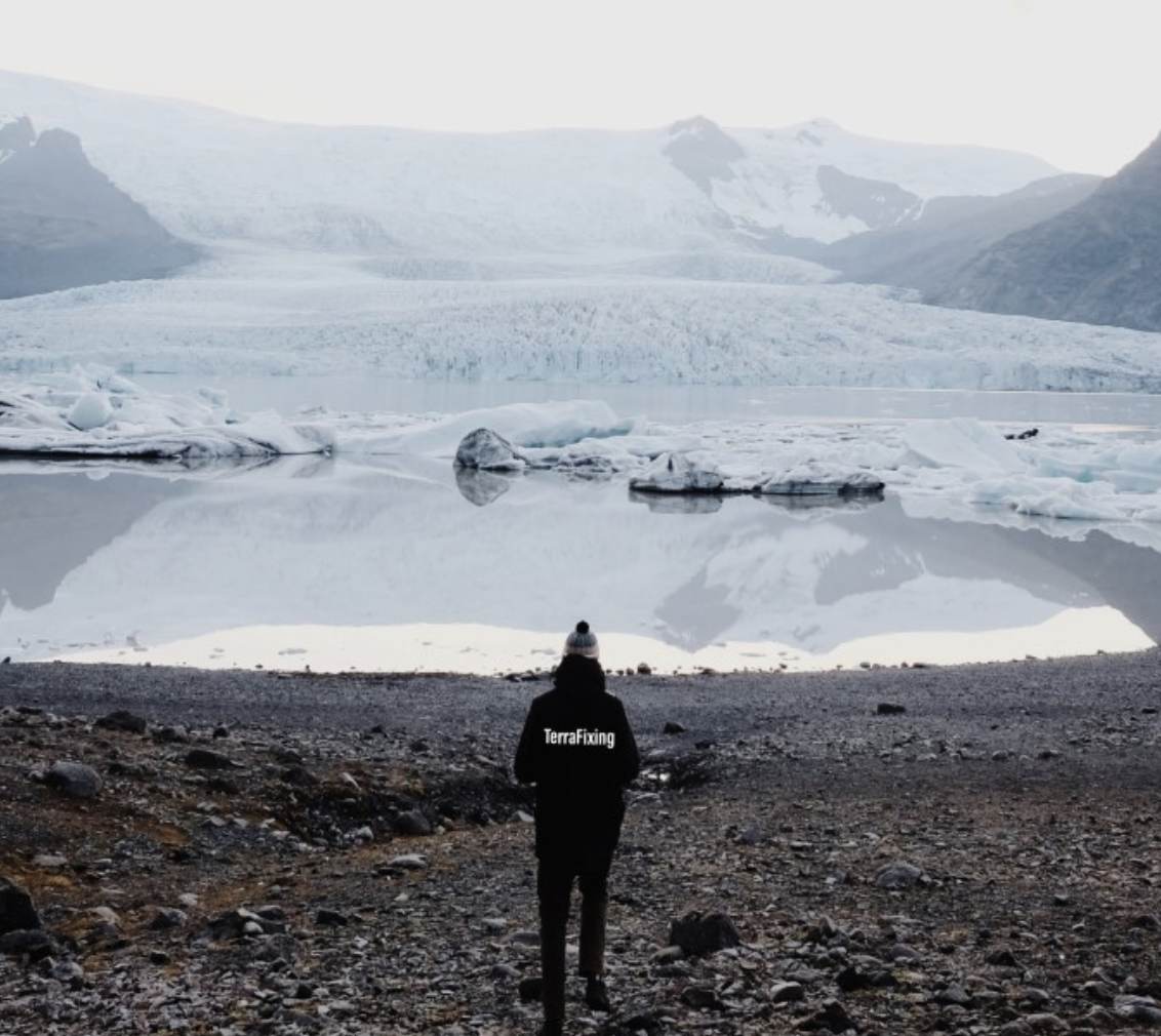 Person in "Storytelling" jacket overlooking a glacial lagoon with icebergs and snowy mountains in the background