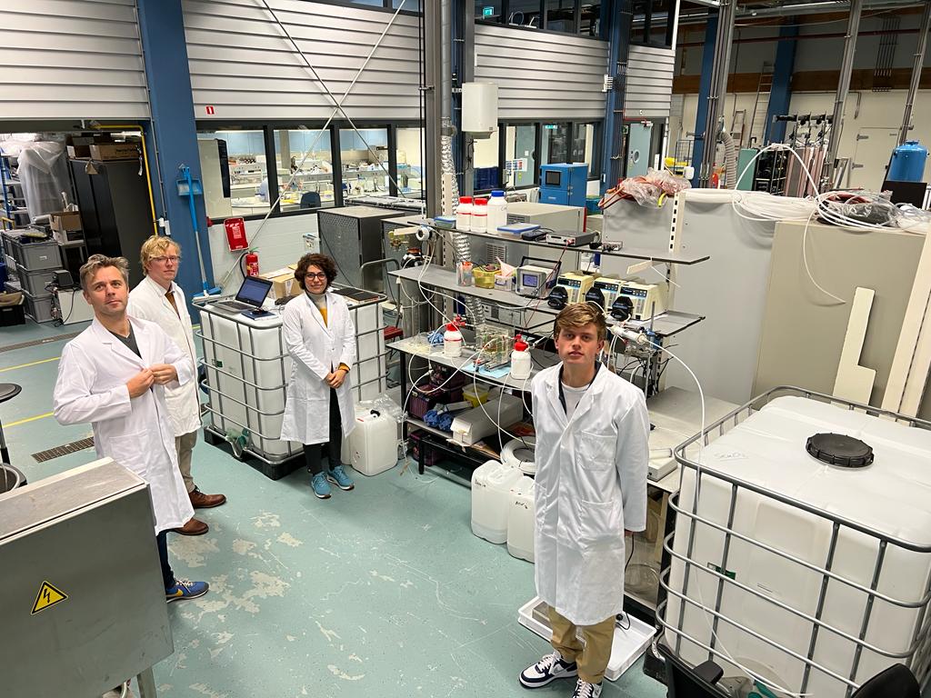 Scientists in white lab coats working in a laboratory with various equipment, containers, and shelving units