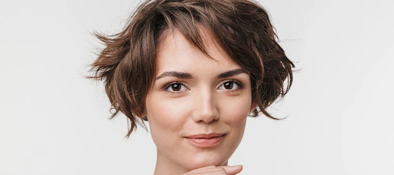 Woman with fair skin and short brown hair smiles in front of a white background