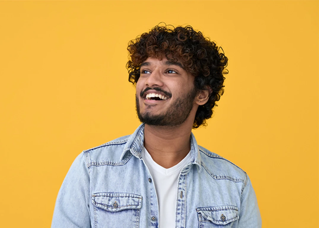 man with curly hairstyle smiling and looking up while wearing denim shirt 