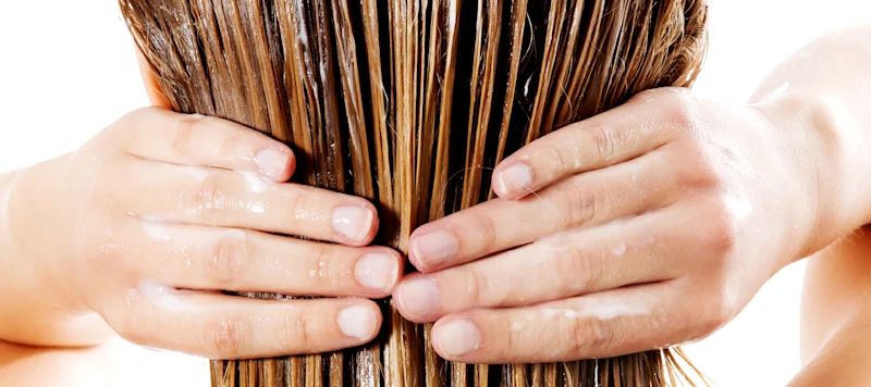 a woman holds her light brown wet hair with both of her hands as she cowashes it.