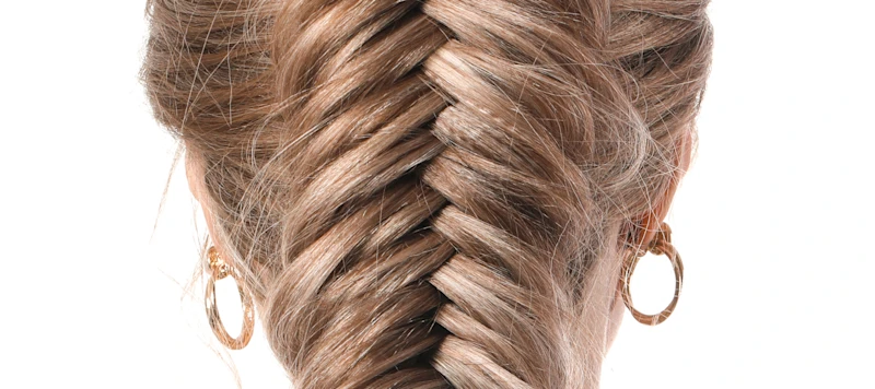 A woman with blonde fish tail braids faces away from the camera in front of a white background.