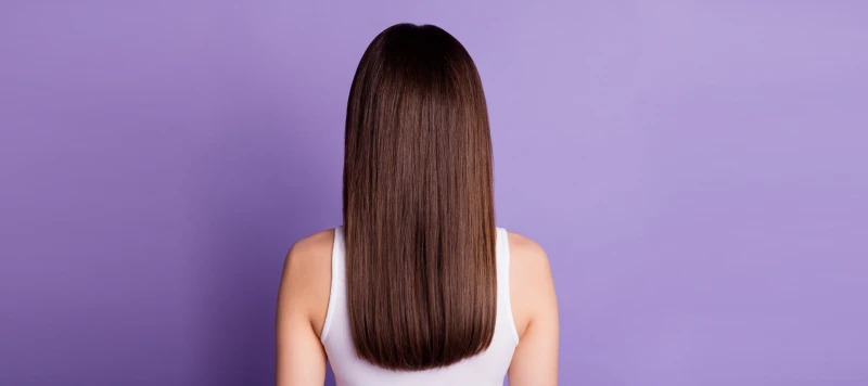 woman with brown straight 1b hair standing with back towards us on a purple background