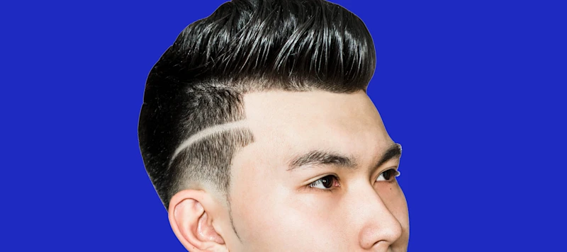 A man with light skin and a pompadour fade haircut looks to the right in front of a blue background.