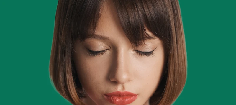 A woman with fair skin and a brown blunt cut bob hairstyle is closing her eyes.