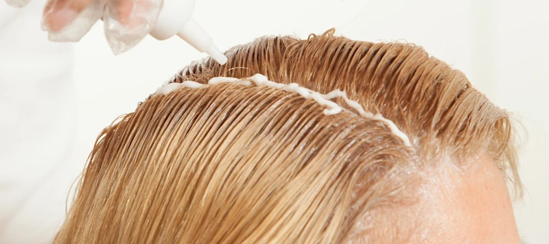 Woman with fair skin and blonde hair has her hair dyed in front of a white background