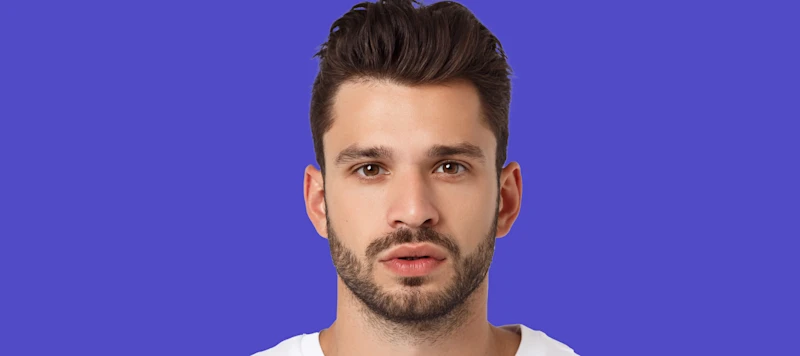 A man with medium length brown hair and a beard looks forward in front of a blue background.