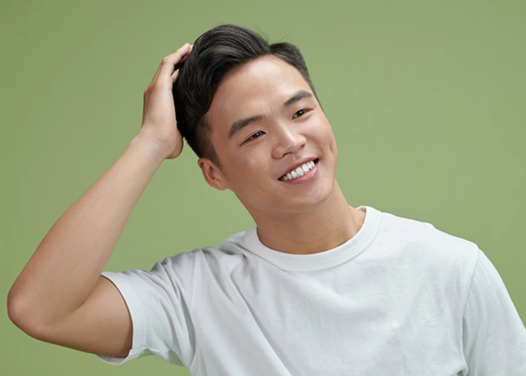 Man smiling while wearing a white shirt and running a hand through his hair