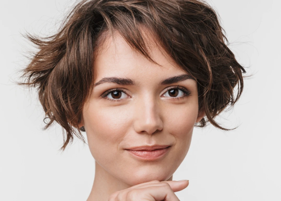 Woman with fair skin and short brown hair smiles in front of a white background