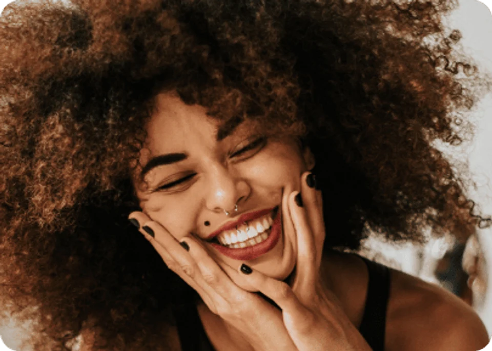 Pretty African American girl with poofy 3b curly hair smiling with eyes closed. Grey background