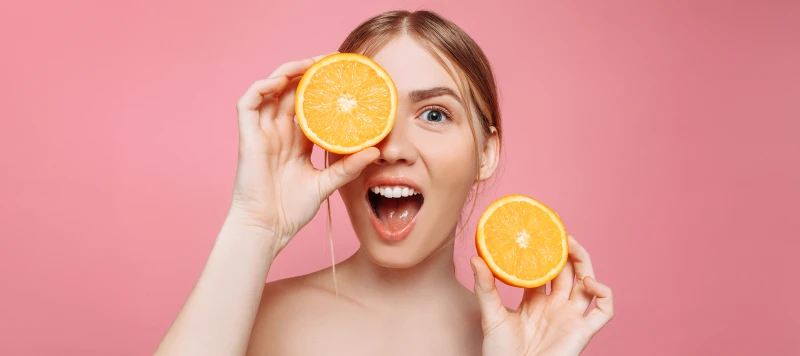 Portrait of a cheerful young woman, with orange slices alluding to Vitamin C, isolated on a pink background. Hair care