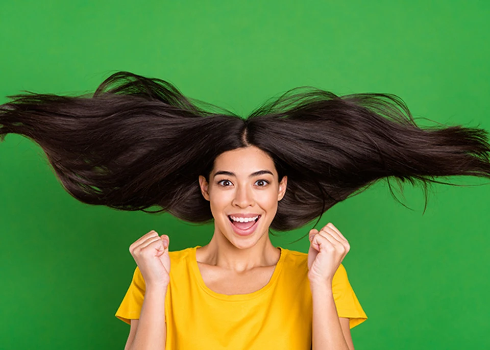 Portrait of girl with long brunette hair gesturing overjoyed with great healthy clean hair isolated on bright green color background