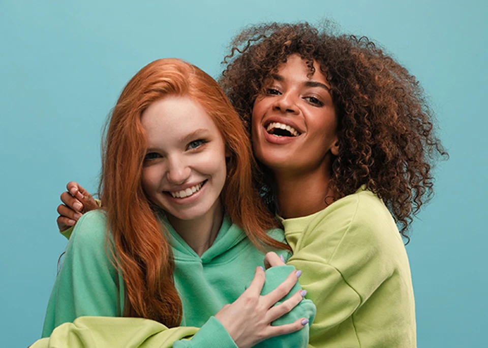 Young woman with textured natural curls and smiling woman with red hair in friendly embrace.