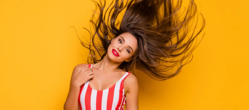 Lady with flowing long hair in a one piece bikini on a yellow background