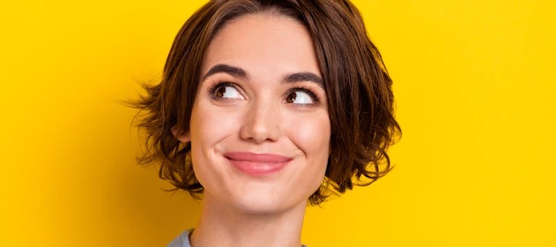A woman with fair skin, a square face and short brown hair grins while looking up in front of a yellow background.