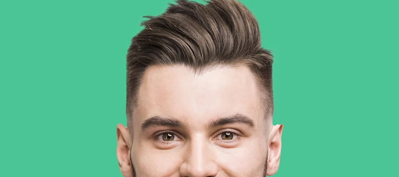 A man with fair skin, brown hair and a side part looks forward in front of a green background.