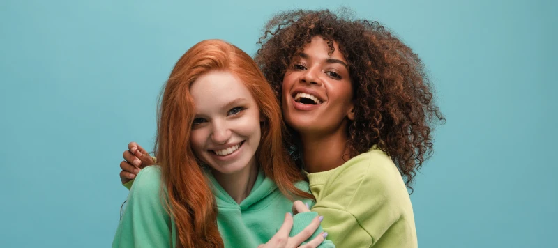 Young woman with textured natural curls and smiling woman with red hair in friendly embrace.