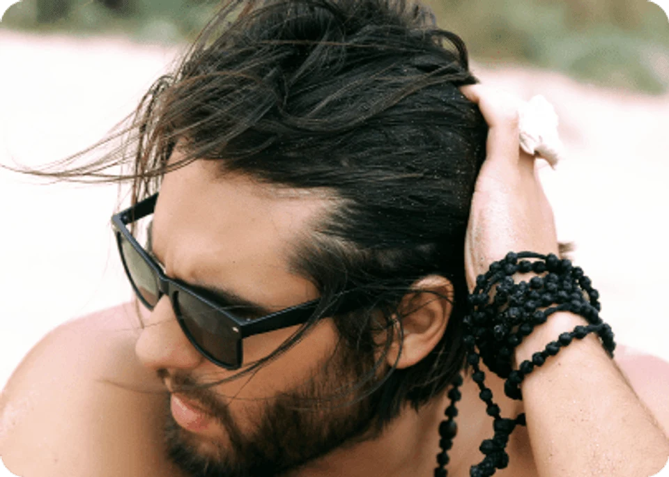 Portrait of hipster man with 1a straight hair in sunglasses and beard posing on the beach