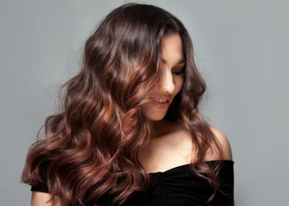 woman with long brown wavy hair smiling looking down in front of a grey background