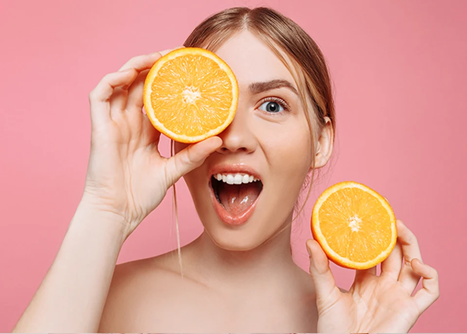 Portrait of a cheerful young woman, with orange slices alluding to Vitamin C, isolated on a pink background. Hair care