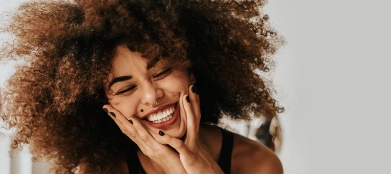 Pretty African American girl with poofy 3b curly hair smiling with eyes closed. Grey background